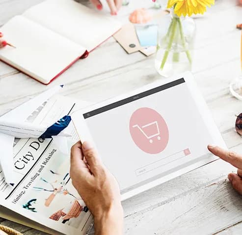 Hands holding a tablet showing an online store page with a shopping cart icon and a search bar