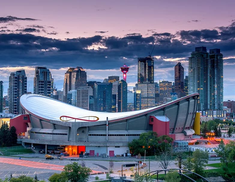 The Scotiabank Saddledome and the downtown Calgary skyline, including the Calgary Tower, lit at dusk