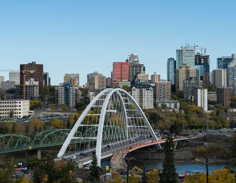 The white steel arches of the Walterdale Bridge over the North Saskatchewan River, with the downtown Edmonton skyline behind it in autumn