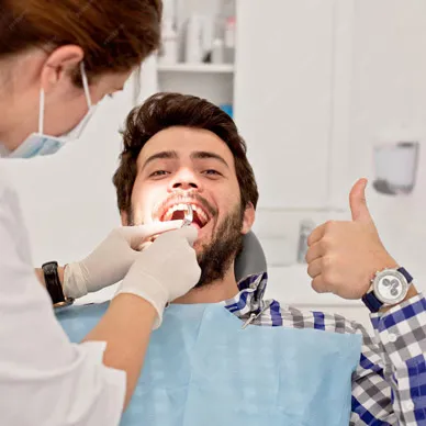 A masked dentist examining a seated patient, who gives a thumbs-up.