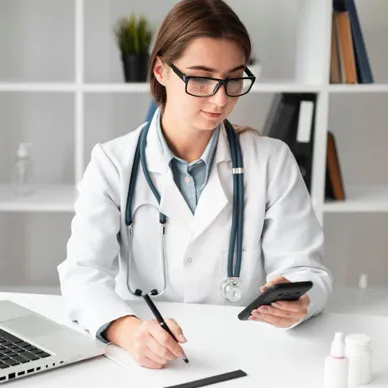 A doctor in a white coat and stethoscope making notes at a clinic desk.