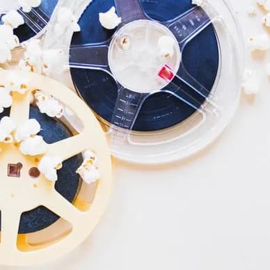 Two reels of film in a clear case on a white surface, scattered with popcorn.