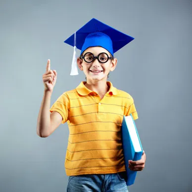 A grinning boy in a graduation cap and round glasses holding a folder and raising one finger.